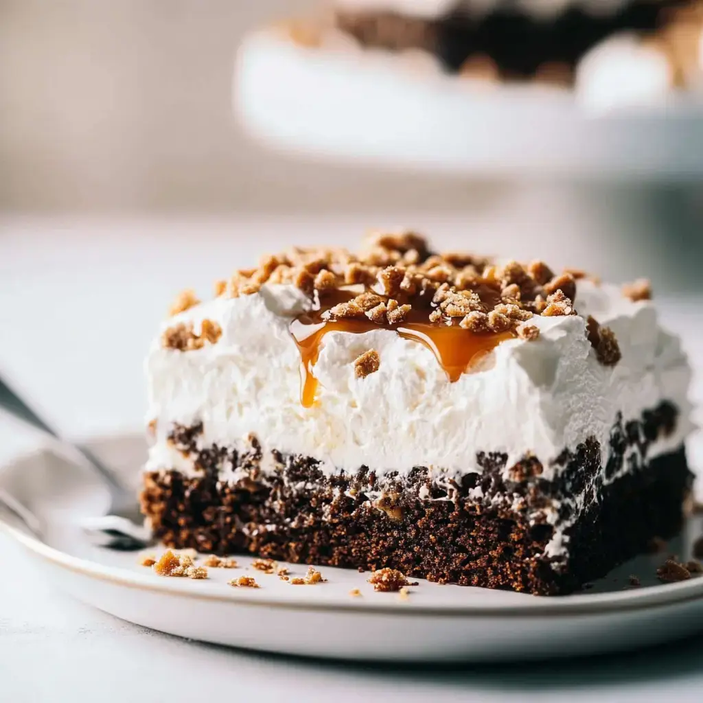 Ein Stück Schokoladenkuchen mit Schlagsahne und Karamell beträufelt, garniert mit zerkleinerten Keksen, auf einem weißen Teller.