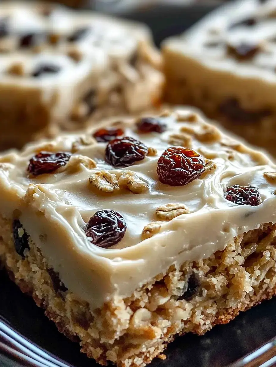 Eine Nahaufnahme eines Dessert-Stücks mit cremiger Glasur Rosinen und Haferflocken auf einem dunklen Teller.