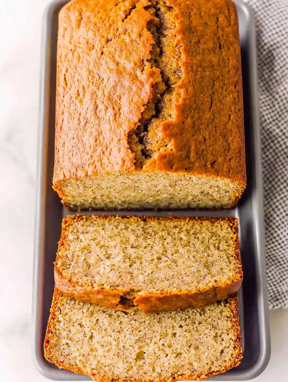 Ein frisch gebackener Brotlaib mit rissiger Oberseite und mehreren abgeschnittenen Scheiben, präsentiert auf einem grauen Tablett.