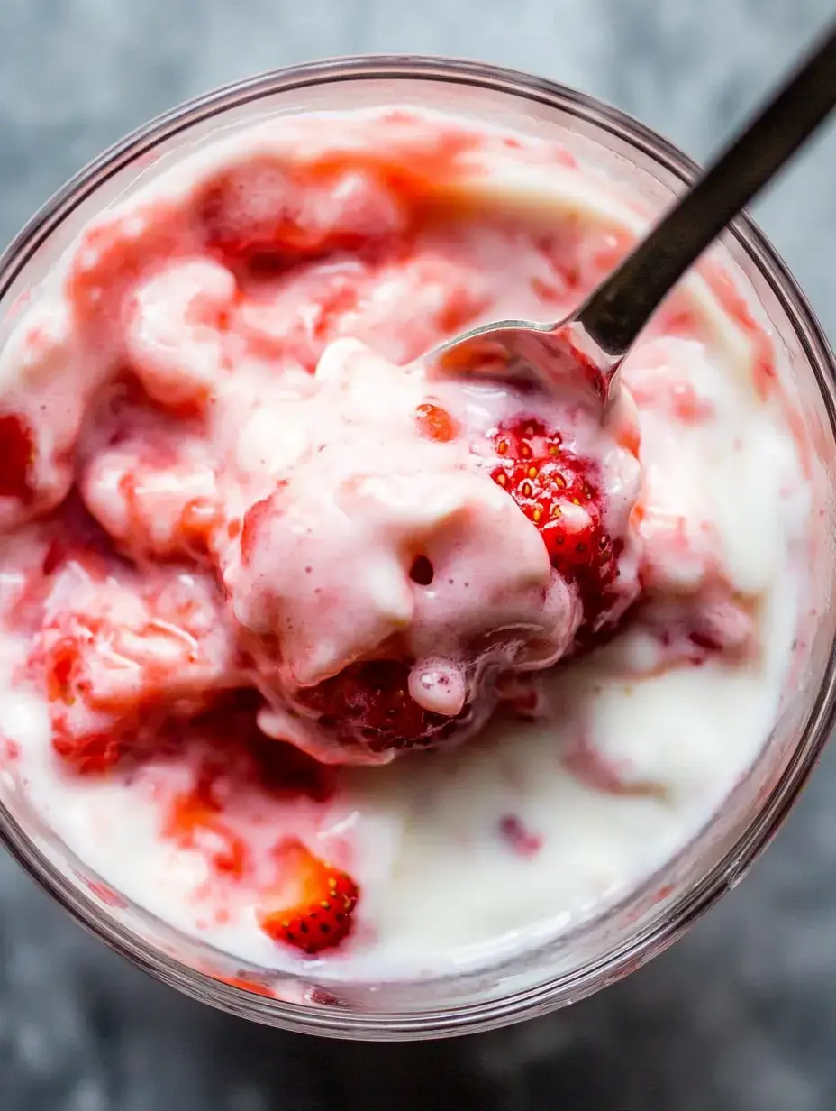 Eine Nahaufnahme einer Schüssel gefüllt mit cremigem Joghurt gemischt mit frischen Erdbeeren und einem Löffel, der darin ruht.