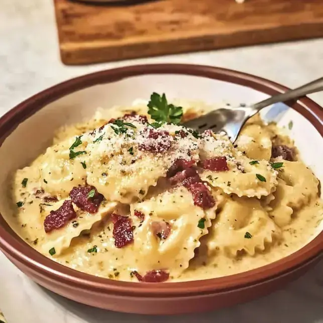 Eine Schüssel cremige Pasta mit knusprigen Baconwürfeln, frisch geriebenem Käse und Petersilie obendrauf.