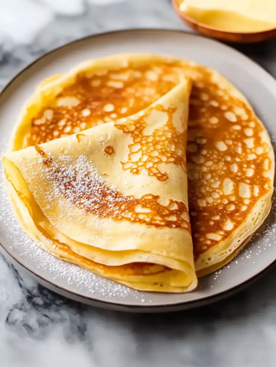 Ein Teller mit frisch gemachten goldbraunen Crêpes, mit Puderzucker bestäubt.